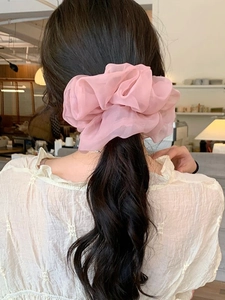 Detailed view of a pink pleated mesh scrunchie styling long dark wavy hair for women