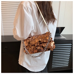 Modern gold sequin handbag with chain strap shown on a model in a minimalist setting
