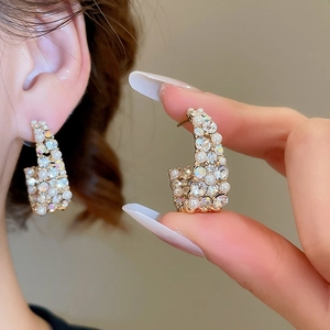 Close-up of C-shaped earrings with inlaid crystals and pearls worn by a model