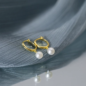 Macro detail of elegant gold hoop earrings with round white hanging pearls on fabric