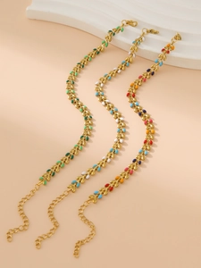 Détail d'un bracelet doré à maillons feuilles et émail multicolore sur fond rose doux
