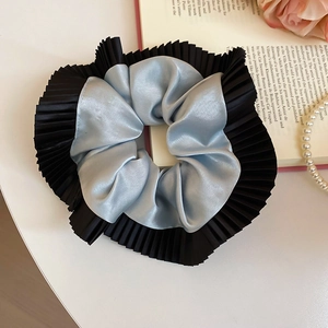 Détail d'un chouchou en soie bleu clair avec des bords plissés noirs sur table blanche