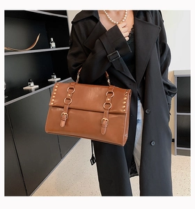Detailed side view of brown leather bag with metallic rivets and decorative straps