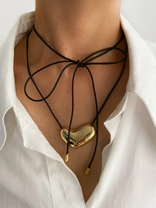Detail of a polished 14K gold heart pendant on a black cord necklace with bow styling
