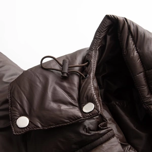 Details der glänzenden dunkelbraunen Steppjacke mit Kordelzug und Metalldruckknöpfen