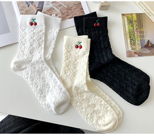 Close-up of cable knit socks with red cherry embroidery in white, beige, and black