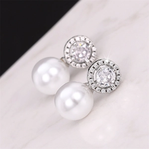 Detailed close-up of pearl earrings with micro-set cubic zirconia on marble background