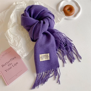 Detailed macro view of soft purple fringe scarf with woven brand tag on white surface