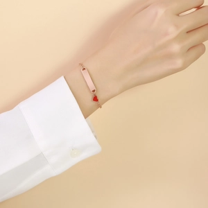 Détail d'un bracelet en or rose avec barre rectangulaire et pendentif cœur rouge au poignet