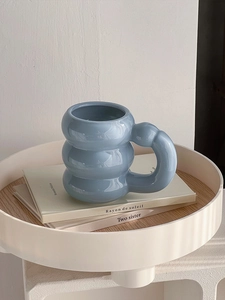 Close-up of blue ceramic mug with unique ringed design and large handle on a white tray