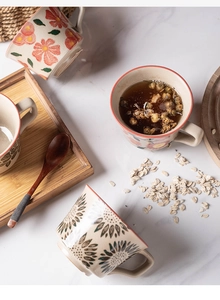 Flat lay of ceramic mugs with red floral patterns, wood tray, and spoon on marble