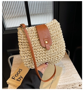 Close-up of woven straw shoulder bag with brown leather strap and fold-over buckle flap
