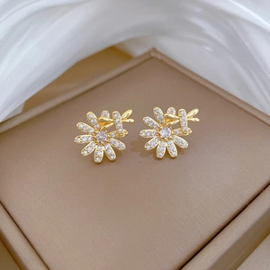 Macro view of gold daisy earrings with insect detail and sparkling crystals on silk