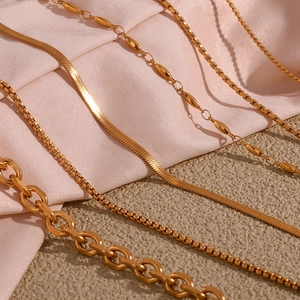 Detail of 18K gold-plated stainless steel snake and box chain necklaces on pink silk