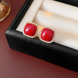 Macro detail of red square zircon earrings with gold plating on beige leather jewelry box