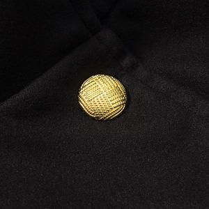 Nahaufnahme eines goldenen strukturierten Knopfes auf einem schwarzen Wollmantel