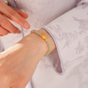 Detail of beaded jadeite bracelet with yellow barrel bead and gold pendant on wrist