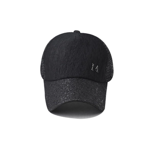 Detail of black trucker hat showing sequin brim texture and silver metal M logo