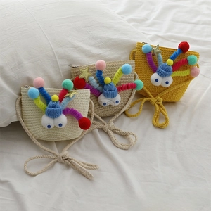 Close-up of cute woven straw mini bags with cartoon eyes and plush ball details