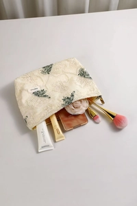 Detail of embroidered floral patterns on cream cotton linen makeup bag with gold zipper