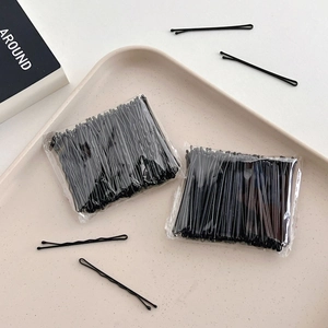 Flat lay of bulk black metal bobby pins for hair styling on a beige display tray