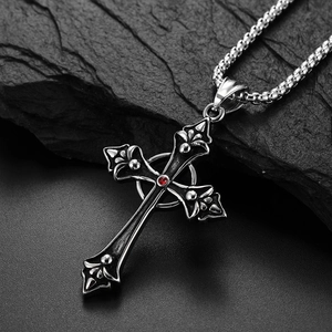 Vintage stainless steel cross necklace with red gemstone pendant on textured stone