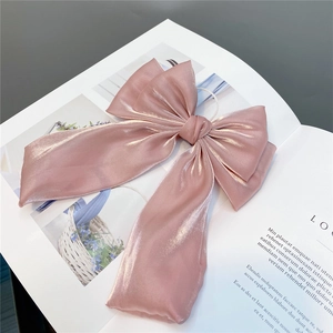 Detailed view of large pink silk bow hair clip with long ribbons on a magazine