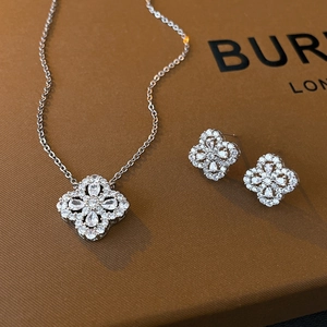 Close-up of sparkling zircon four-leaf clover necklace and stud earrings set on leather