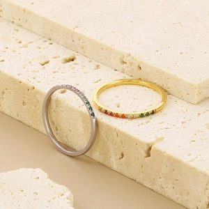 Close-up of gold and silver minimalist rings with colorful rainbow stones on beige stone