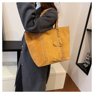 Close-up of yellow-brown suede tote bag featuring rivet straps and heart charm detail