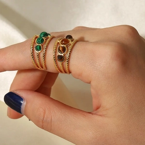 Dettaglio di anelli a corda dorati con pietre di malachite verde e occhio di tigre