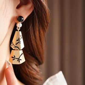 Detail of golden geometric earring with bamboo pattern and pearls worn by a model