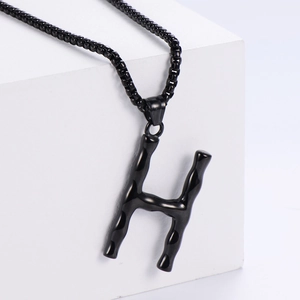 Gros plan du pendentif lettre H noir 3D avec texture bambou sur une chaîne à mailles
