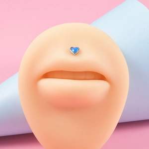 Macro shot of heart-shaped blue opal labret stud set in a silver base on a silicone lip