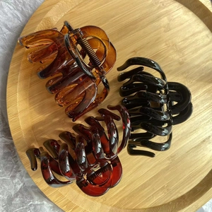 Three oversized glossy hair claws in amber, black, and dark red on a wooden tray
