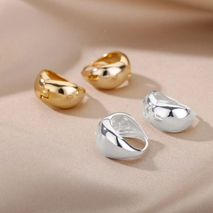 Detail of chunky gold and silver oval hoop earrings on beige satin with high polish finish