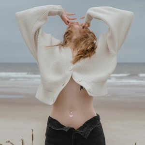 Detailed close-up of a pink heart-shaped crystal navel ring on skin at the beach