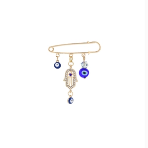 Macro shot of gold Hamsa hand and blue evil eye charms dangling from a metal brooch