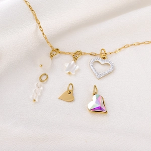Detailed shot of golden necklace charms with crystal heart and star on silk background
