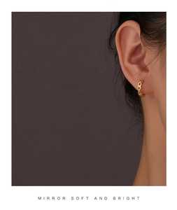 Close-up of golden hollow heart chain earrings worn by model on a dark background