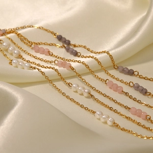 Detailed view of 18K gold plated chains with pearls and beads on beige silk fabric
