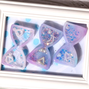 Macro detail of lavender and blue gradient hourglass resin charms with iridescent glitter
