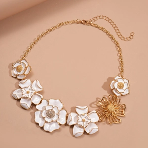 Elegant gold necklace with white enamel flowers and crystals on a soft pink background