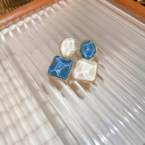 Macro shot of geometric blue and white enamel earrings on a textured glass tray