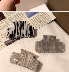Three acetate hair claws with zebra, grey, and marble patterns on linen background