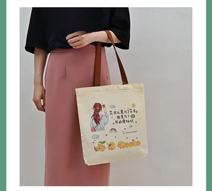 Detail of off-white canvas tote bag featuring brown straps and cartoon illustration