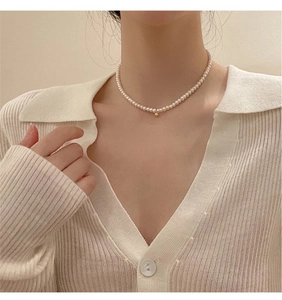 Close-up of a natural pearl necklace with a gold bead worn on a white cardigan