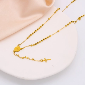 Polished gold beaded cross necklace with a religious medal on white display stand