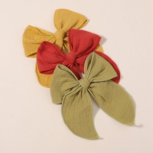 Three large linen bow hair clips in mustard yellow, brick red, and olive green colors