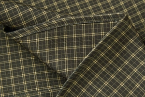 Detail of dark green and coffee plaid fabric with fine yellow lines and neat stitching